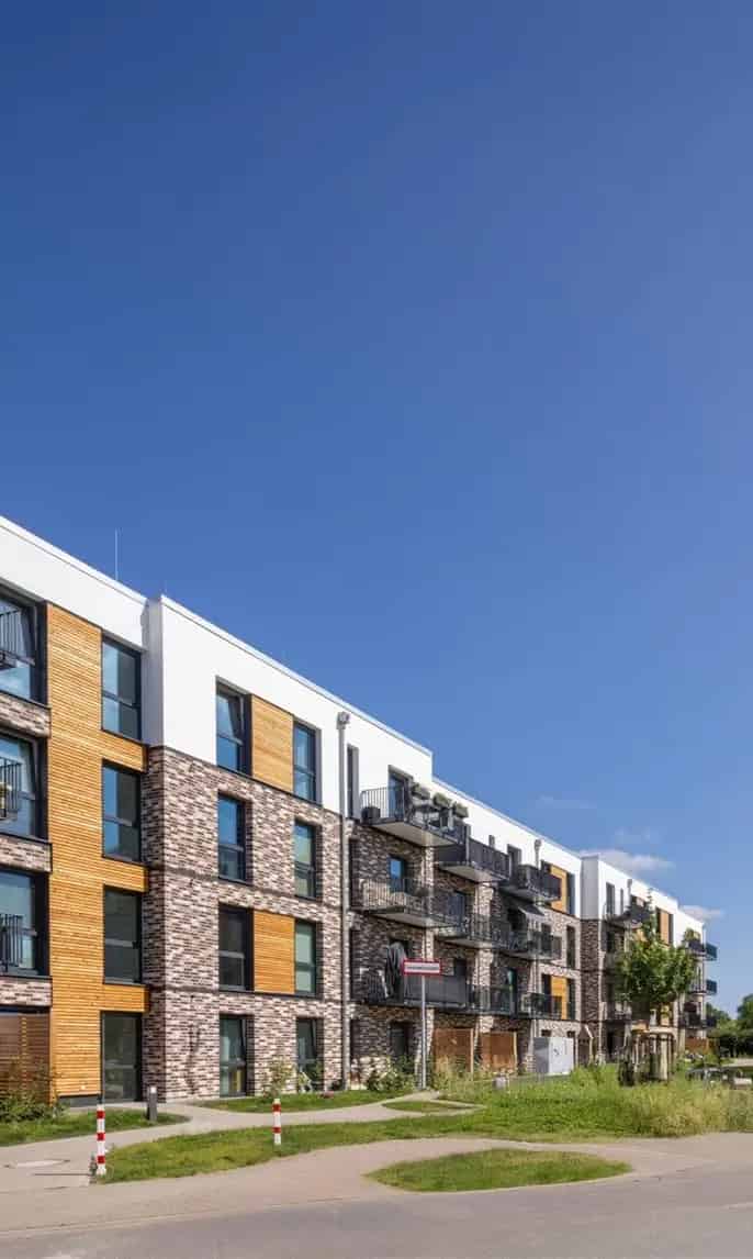 Moderne woongebouwen met meerdere verdiepingen en balkons, omgeven door groene zones en een parkeerplaats op een zonnige dag.