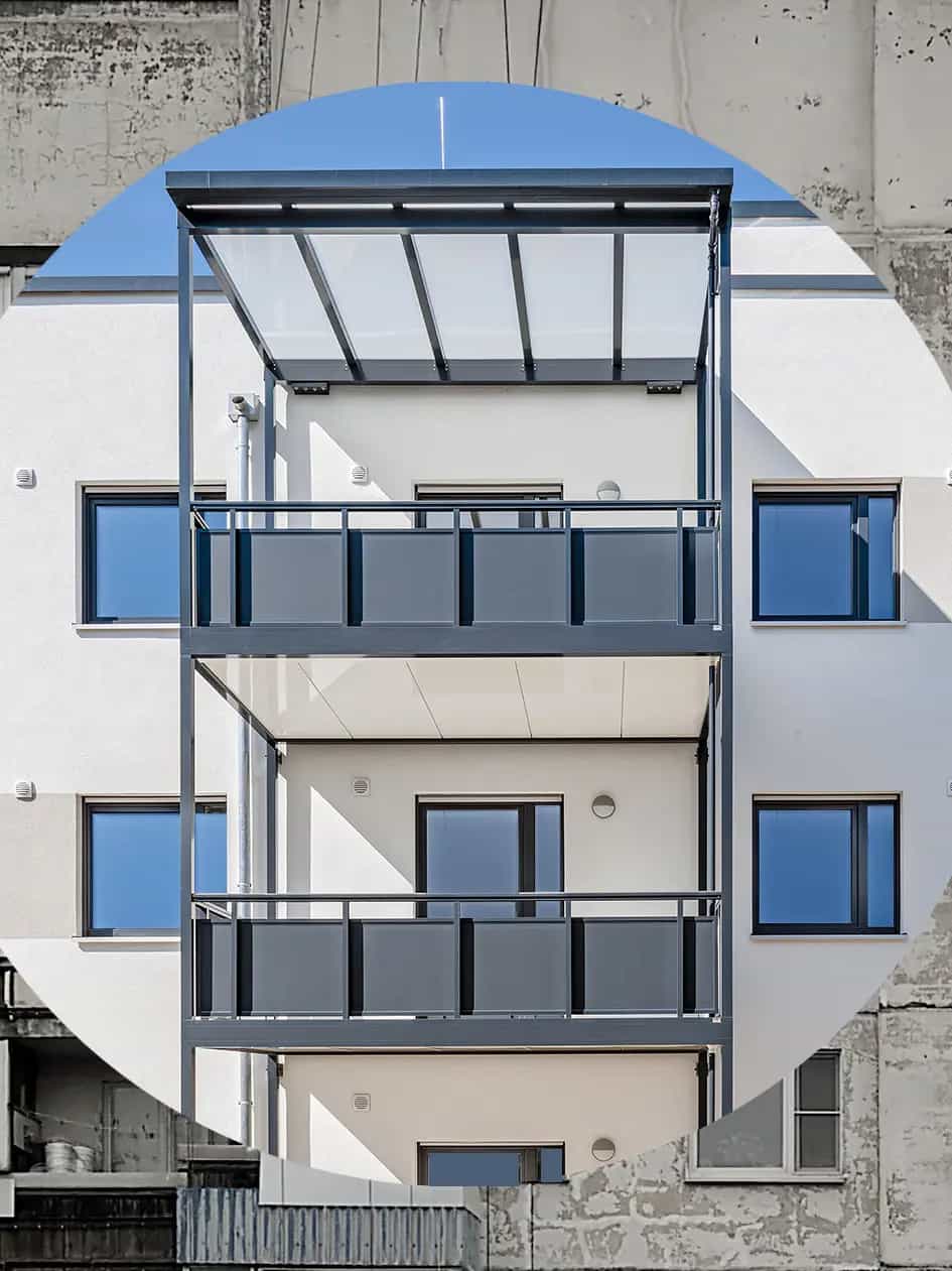 Moderner Balkon eines sanierten Gebäudes vor älterer, unsanierter Fassade.